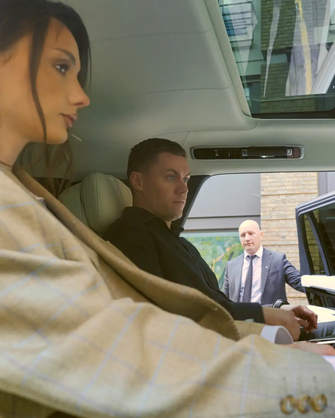 A professional security chauffeur sits in the front seat of a luxury Range Rover while a female executive client is in the back. A second security guard stands outside the open car door, highlighting a comprehensive executive security chauffeur service in London.
