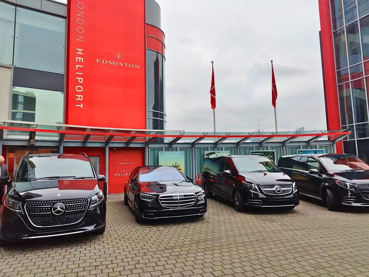 A fleet of uniform black luxury chauffeur vehicles, including a Mercedes-Benz S-Class and multiple Mercedes-Benz V-Class MPVs, parked in front of the London Heliport Edmiston terminal.