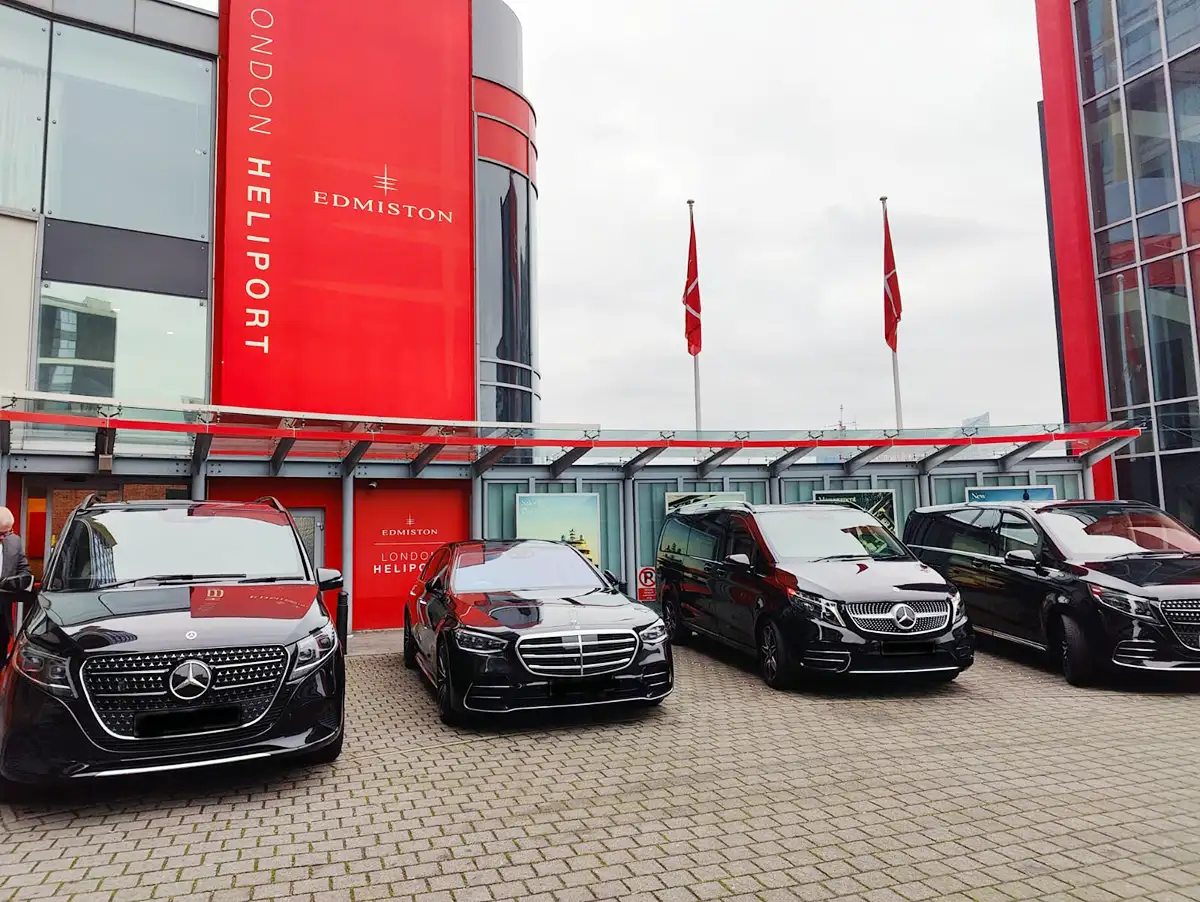 Four black luxury Mercedes-Benz vehicles, including an S-Class saloon and V-Class MPVs, parked on the forecourt outside the red Edmiston London Heliport building.